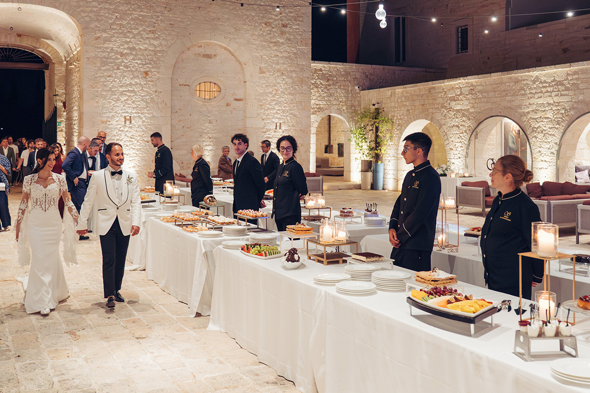 Buffet serale nella corte in pietra della masseria, con sposi, ospiti e staff al servizio.