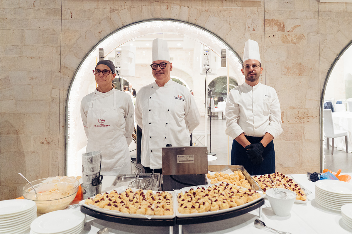 Staff di cucina con chef in divisa, buffet salato e sala con archi in pietra.