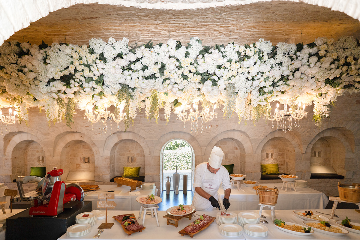 Chef di Relais Il Santissimo in sala ricevimenti con tavoli allestiti per l’evento e fiori.