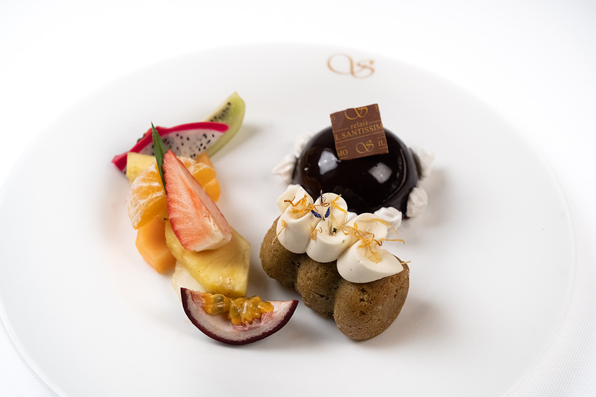 Dessert al piatto con dolce al cioccolato, frutta fresca, creme e decorazioni con logo del ristorante.