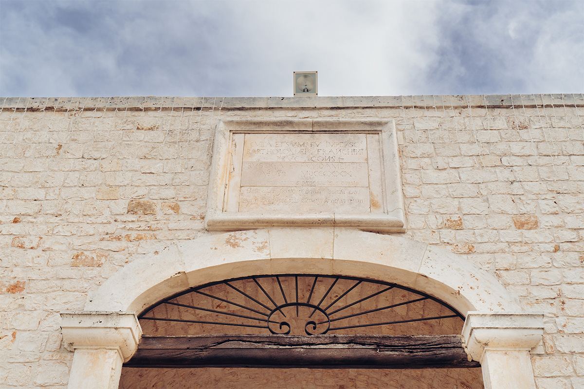 Dettaglio della facciata in pietra della masseria con portale ad arco e antica iscrizione. 