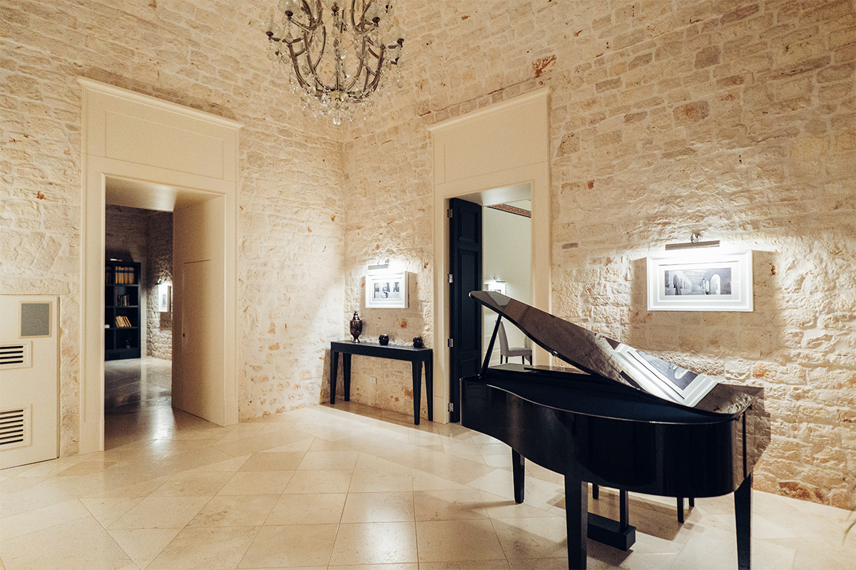 Sala interna in pietra con pianoforte a coda, lampadario e dettagli eleganti.