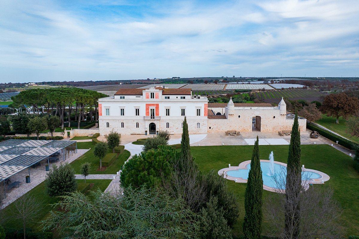 Vista aerea de Il Santissimo, con palazzo storico, corte della masseria, giardini e paesaggio pugliese.