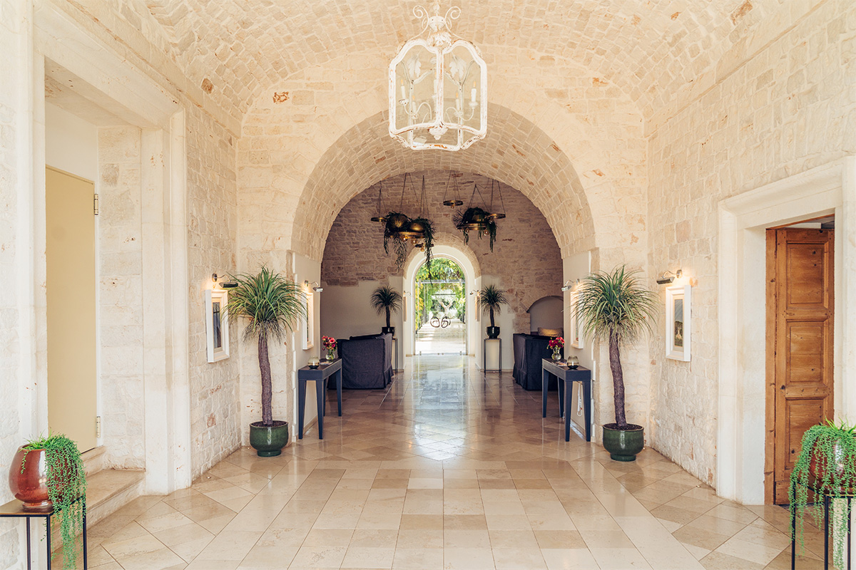 Ingresso dell’hotel Il Santissimo con volte in pietra, piante e lampadario.