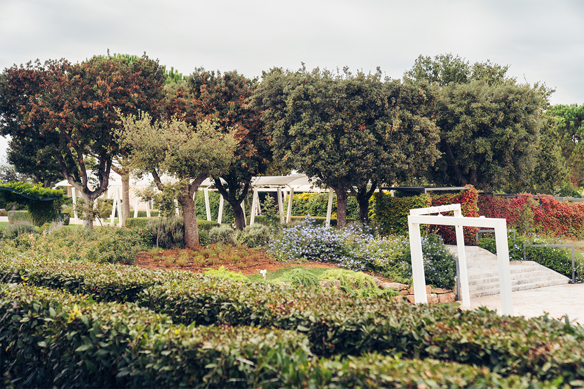 Relais Il Santissimo park area with hedges, trees and white pergolas.