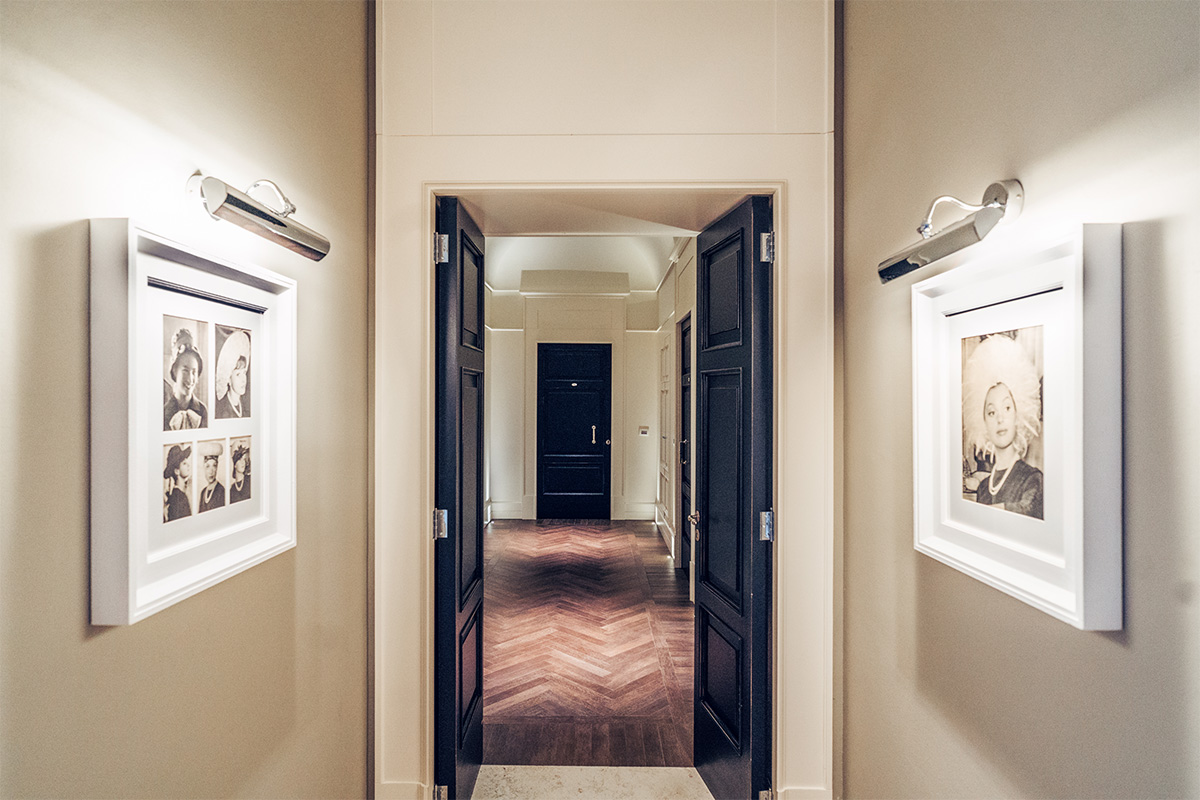 Corridoio dell’hotel con porte scure, quadri alle pareti e pavimento in pietra.