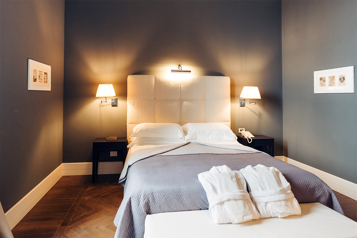 Armonia Deluxe room with double bed, light headboard and soft lighting.