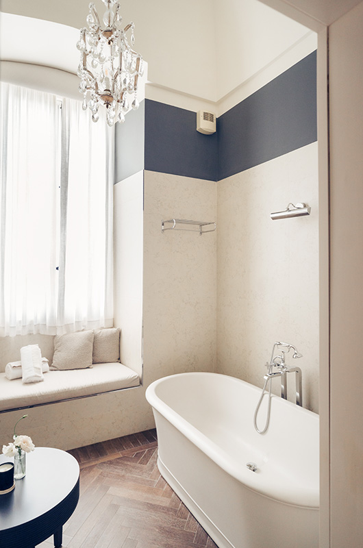 Bagno con vasca freestanding, lampadario e finestra luminosa.