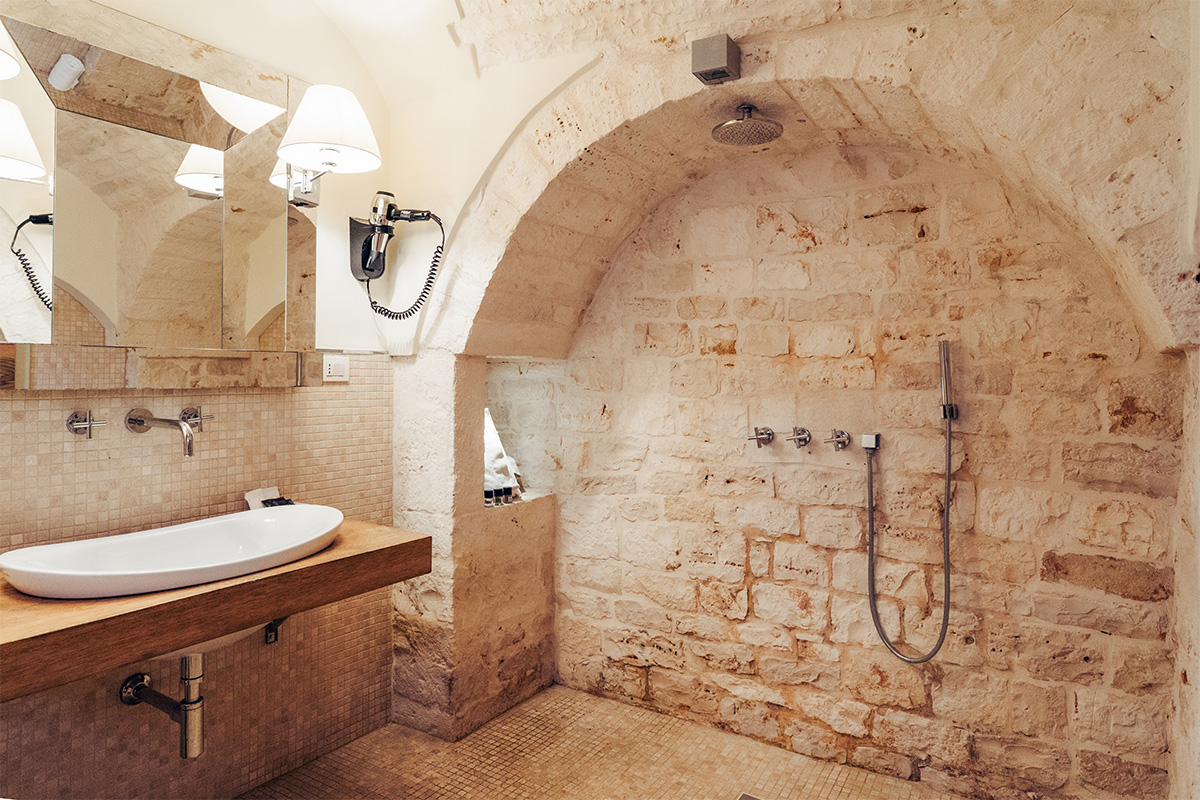 Bagno della Suite del Massaro con lavabo, doccia e pareti in pietra.