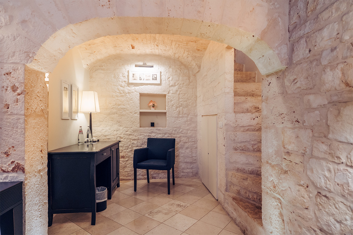 Ingresso della suite con pareti in pietra e arredi d’epoca.