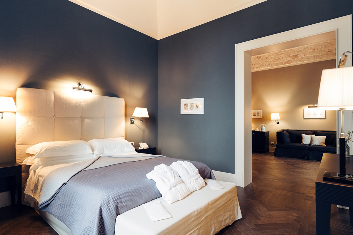 Zona letto della Suite Padronale con letto matrimoniale, parete blu e salotto a vista.