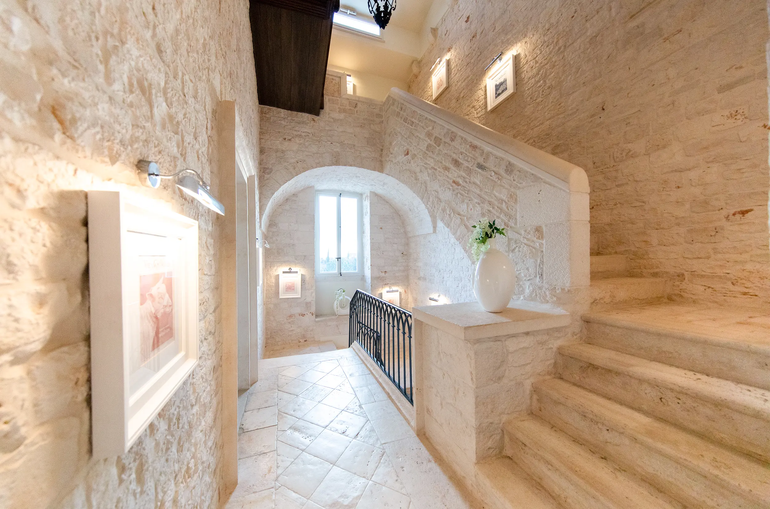Stone staircase in Relais Il Santissimo hotel with arched hallway and framed artworks.