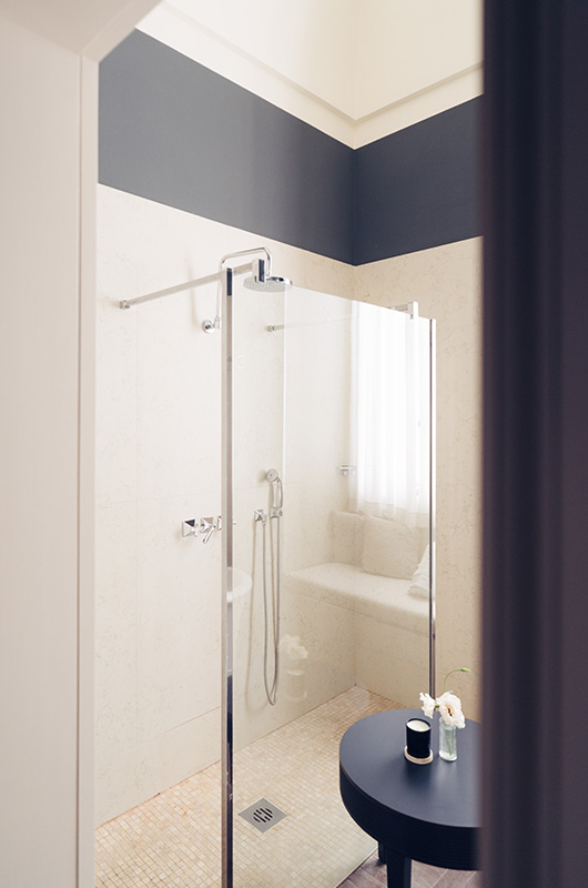 Bathroom with glass shower, dark blue walls and light details.