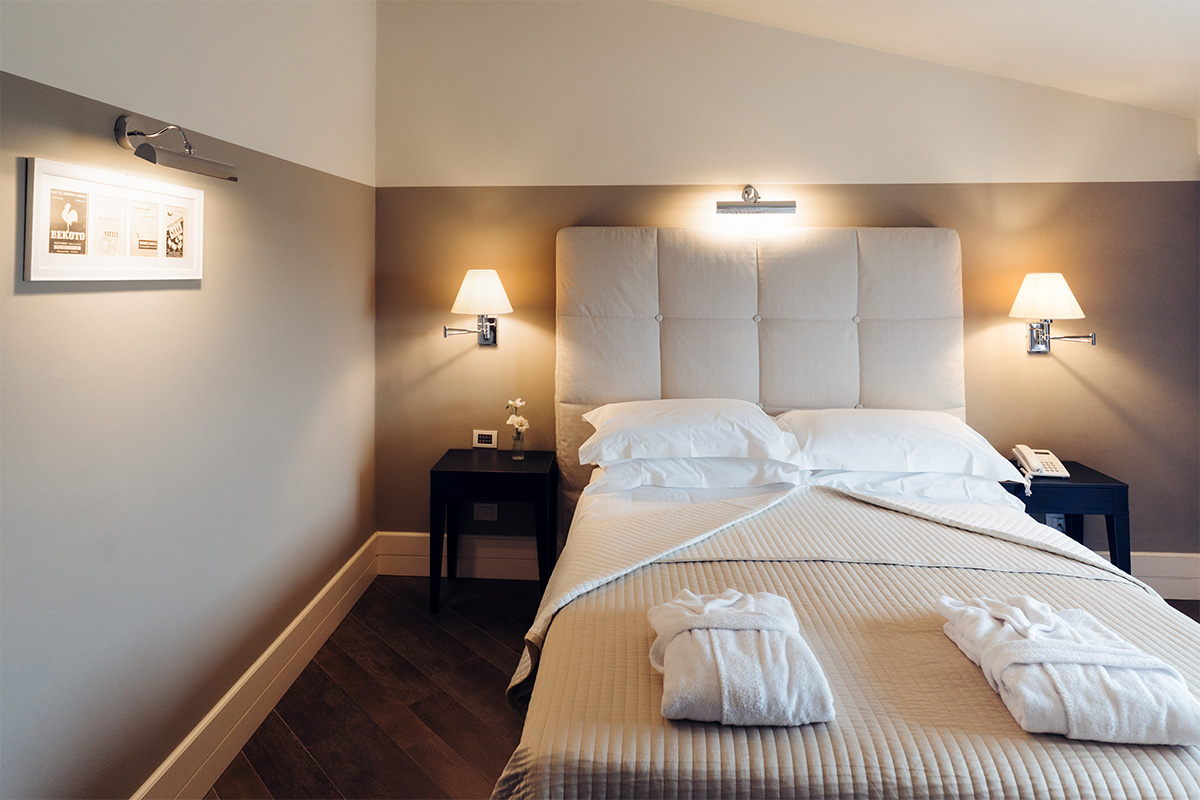 Camera con letto matrimoniale, parete taupe e luci da comodino.