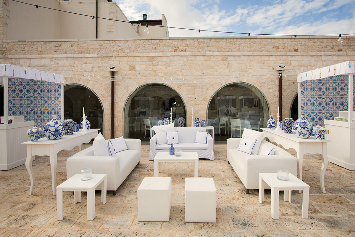 Outdoor event arrangement in Il Santissimo Masseria courtyard with stone arches and blue patterned tiles.