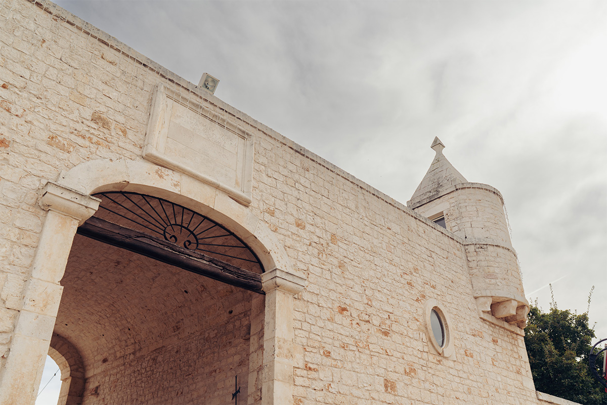 Stone entrance of Il Santissimo Masseria with arched wooden gate and historic Puglian tower.
