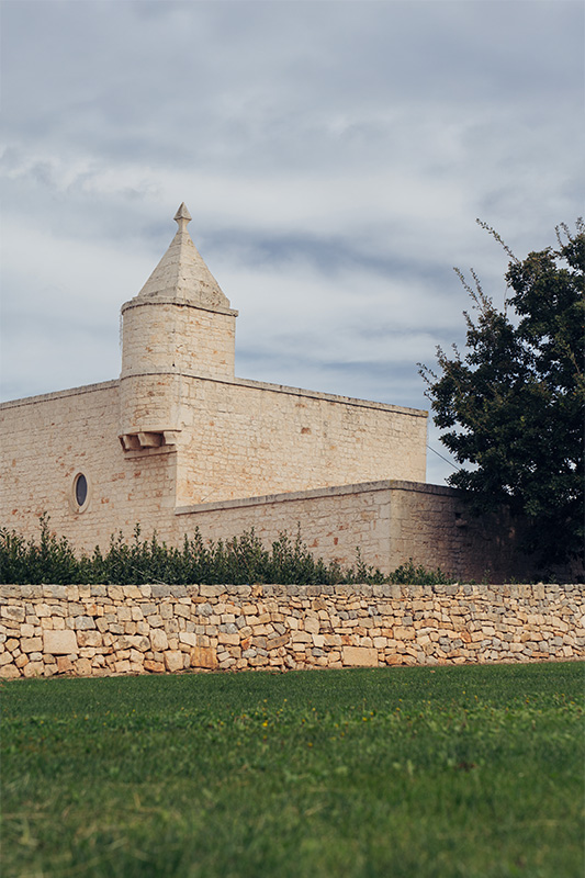 Il Santissimo Masseria exterior with stone walls, green lawn and historic Puglian tower.