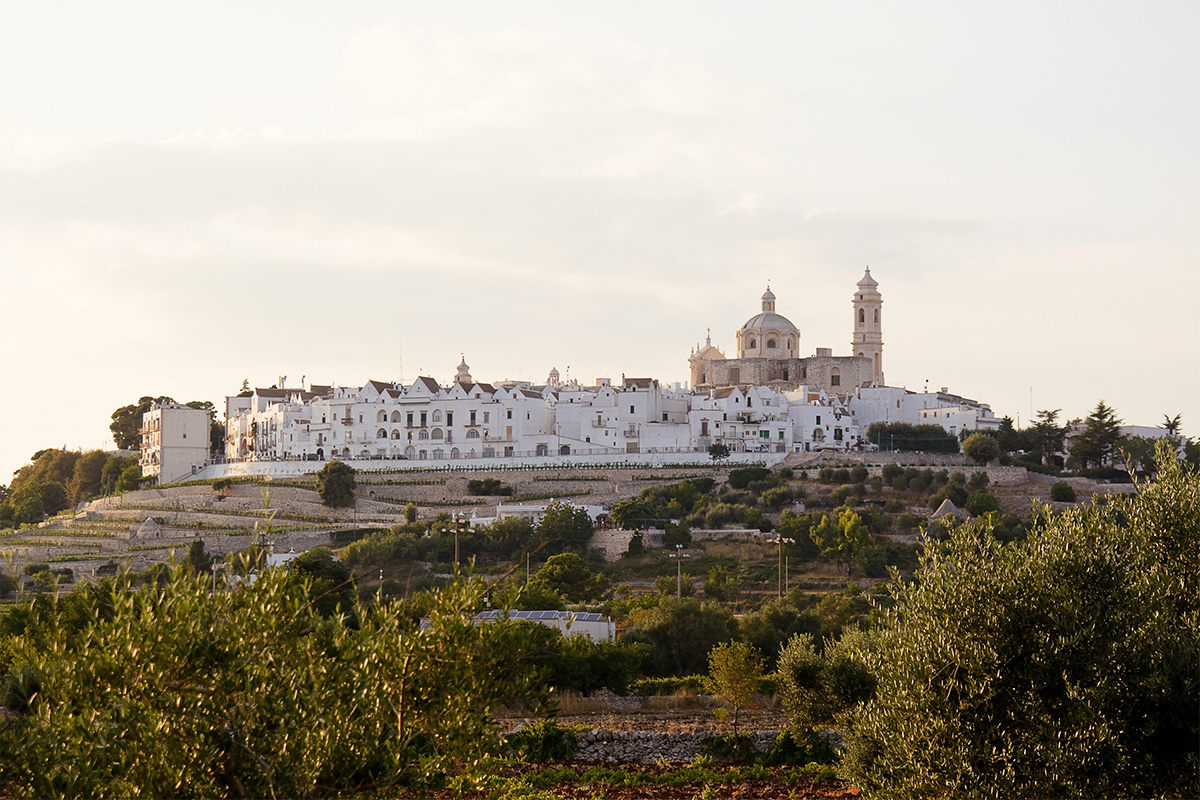 Panoramic view of Locorotondo, with its white historic center on the hill and the Apulian countryside at sunset.