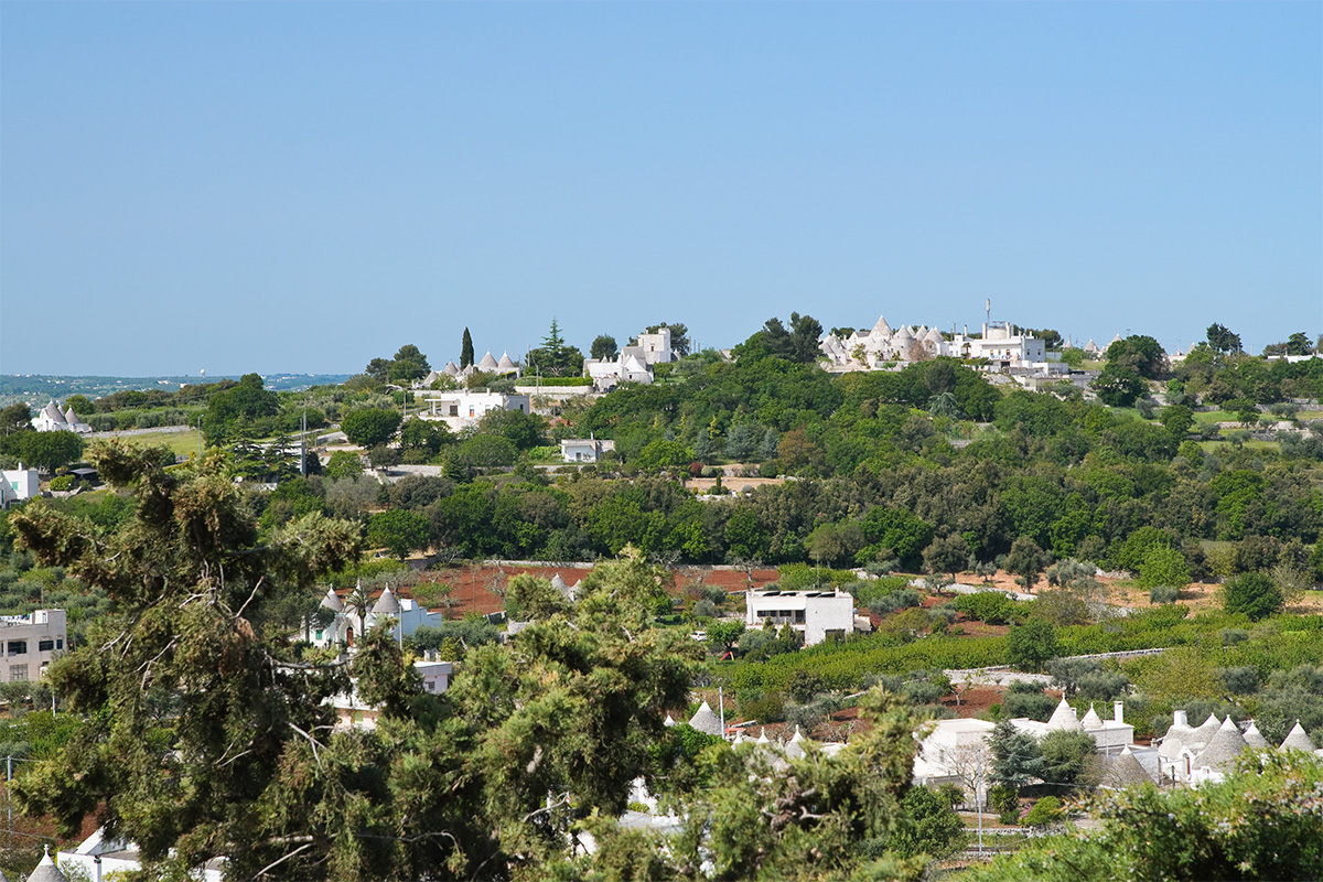 Itria Valley landscape with white trulli and Mediterranean vegetation.