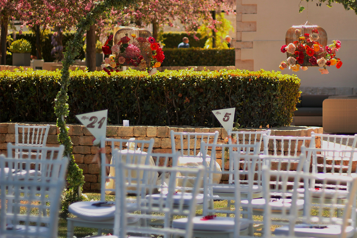 Outdoor ceremony setup, with white chairs and hanging flowers.