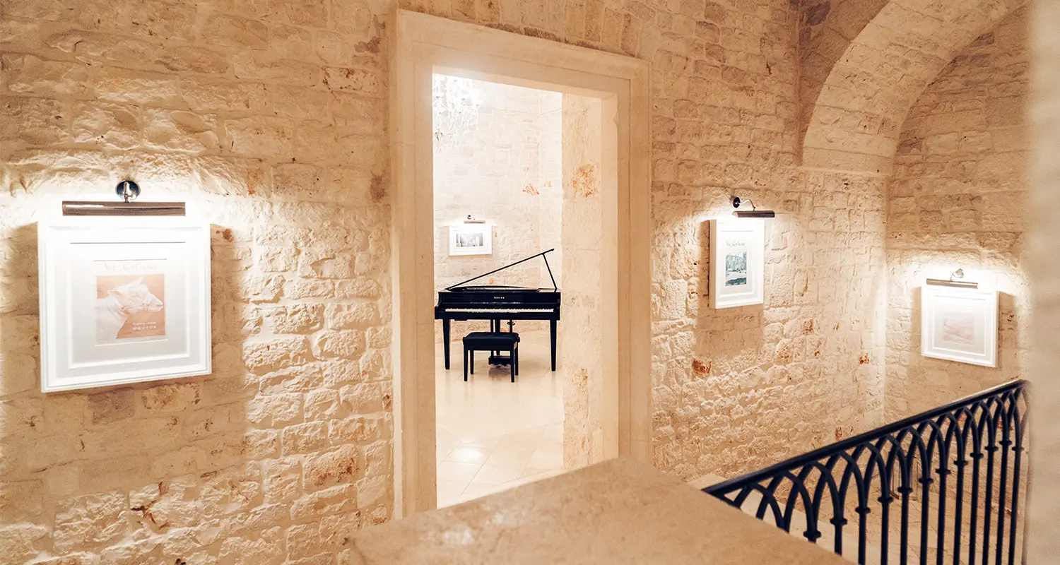 Corridoio in pietra con quadri illuminati e vista sul pianoforte.