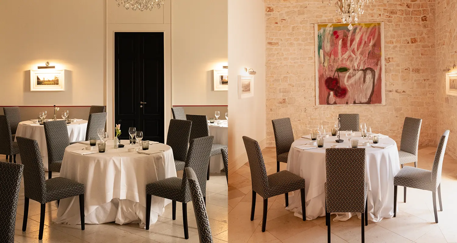 Sala ristorante con tavoli apparecchiati, parete in pietra e quadri.